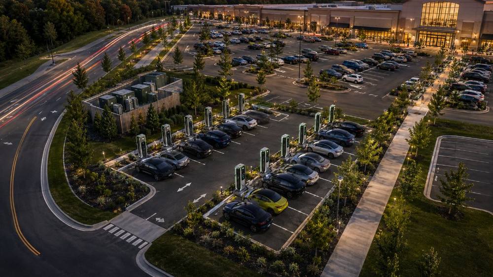 Aerial view of a dedicated DC fast charging plaza within a large retail parking field at dusk